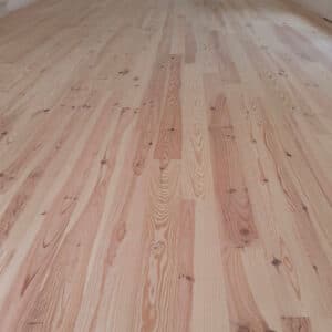Sol en parquet clair fraîchement posé. Lames de bois naturel avec motifs de grain distincts et nœuds apparents. Ambiance lumineuse et propre.