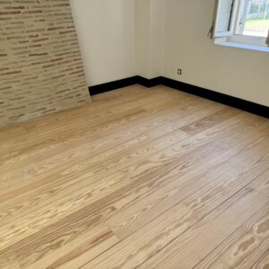 Parquet massif en pin maritime sans noeud largeur 200mm avec plinthes moulurées peintes en noir
