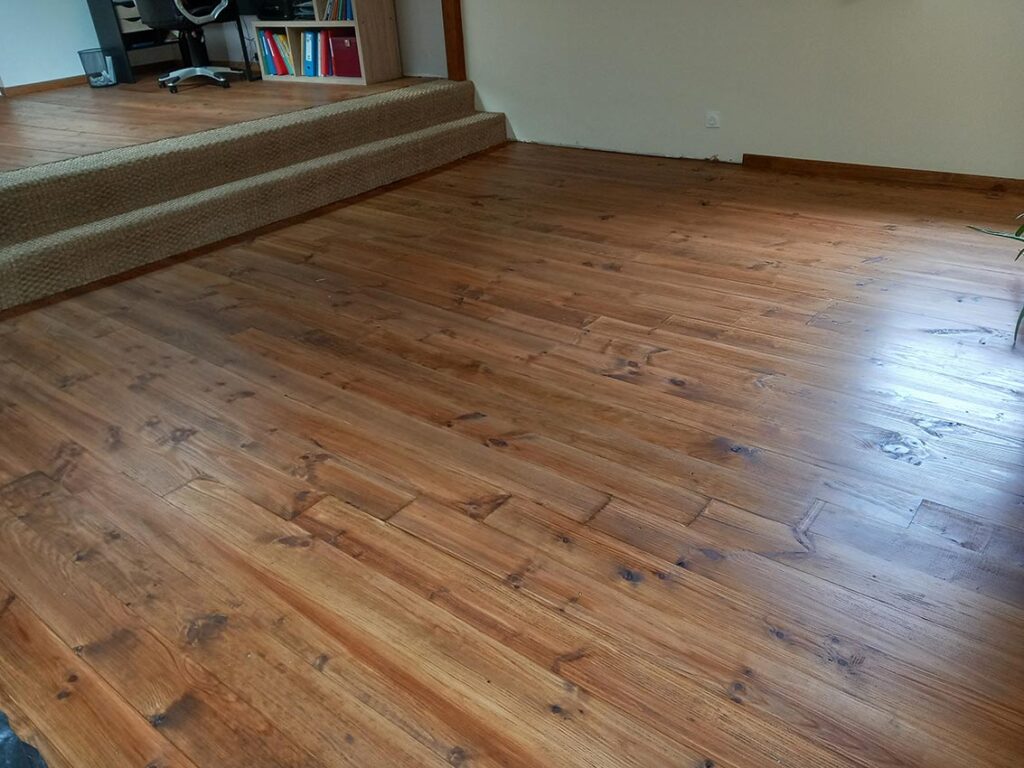 Plancher en pin rustique verni et patiné, menant à deux marches basses recouvertes de moquette beige dans un espace de bureau ouvert.
