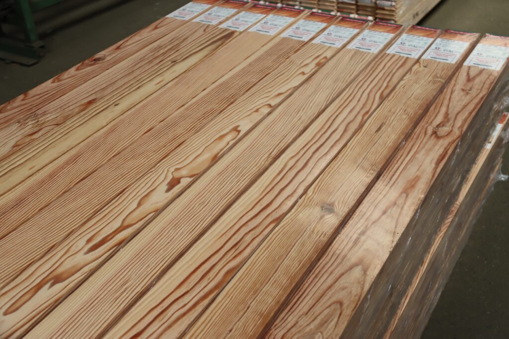 Piles de planches de bois naturel clair empilées, emballées avec leurs étiquettes produit visibles et grains apparents.